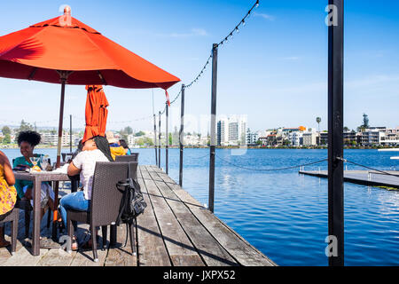 OAKLAND, CA- May 9, 2017: Women dining at a restaurant on Lake Merritt on a wooden dock with orange market umbrellas. Bright sunny afternoon. Stock Photo