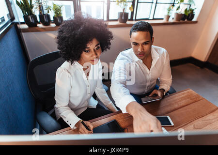 Shot of two young entrepreneurs sitting together and working at office desk. Man and woman working together in office. Stock Photo
