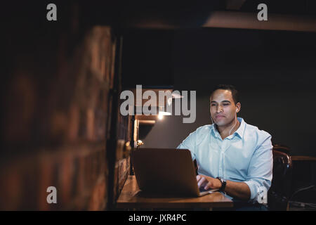 Young man working at the laptop late at night. African businessman working overtime in the office. Stock Photo