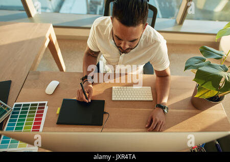 Top view shot of young man working in office using graphics tablet and computer. Male creative profession at his work desk. Stock Photo