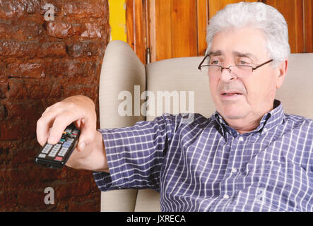 Portrait of an old man using remote control and watching tv. Indoors. Stock Photo