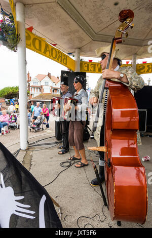 England, Broadstairs folk week. Folk group, Stowfolk, performing on the bandstand. Side view, close up of cello being played by one member of the group, the others in background playing accordion. Group wearing pirate costumes. Daytime. Stock Photo