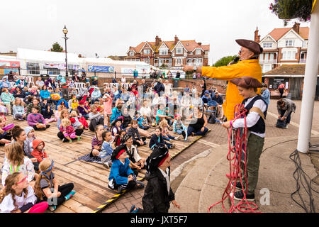 Popular Outdoor Hobby Horse Club, Mick Scott hosting the show in front of an audience of children during Broadstairs Folk Week. The theme is pirates with many dressed in pirate outfits and hats. View from side of bandstand of Mick and his young helper with audience in front of them. Stock Photo