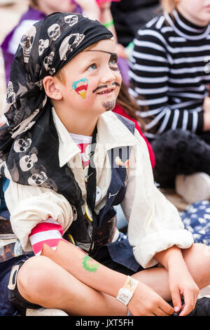 England, Broadstairs folk week. Hobby Horse Club. Young boy child, sitting in audience, wearing black pirate costume and eye-patch watching and concentrating with smile on his face looking up. Stock Photo