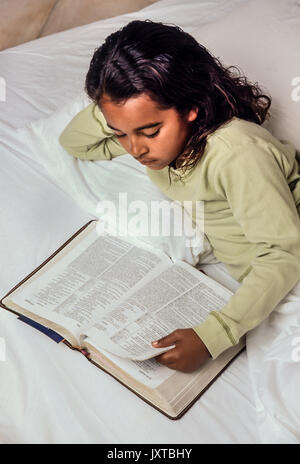 Childhood Ethnic child reading Bible in bed Young Girl 7-10 year old  African American/Caucasian United States Myrleen Pearson Stock Photo