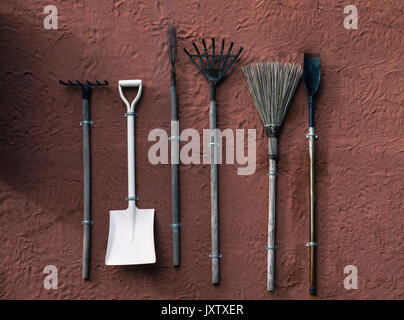 Broom, shovel, rake,spade hang on orange cement wall,Garden equipment groundworks hang on the red wall Stock Photo