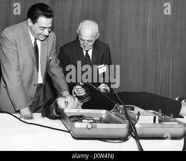 William Bennett Kouwenhoven, Candid photograph, Demonstrating the cardiac defibrillator which he invented on a well dressed woman lying on a table, while a man looks on, 75 years of age, 1962. Stock Photo