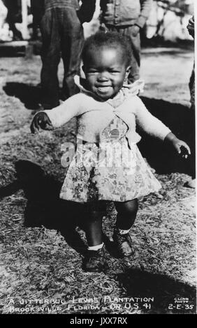 A young African American girl in a floral dress and a sweater smiling and running outside on the Lewis Plantation in Brooksville, Florida, 1940. Stock Photo