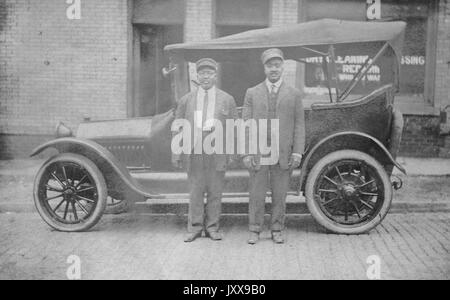 Two African American men wearing suits and hats in front of a car, in front of a dry cleaning shop, neutral facial expressions, 1920. Stock Photo