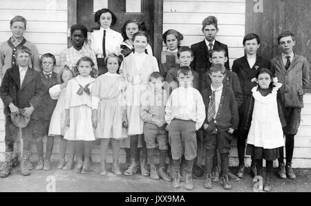 Full length landscape shot of schoolchildren, standing outside building, one African American student, 1920. Stock Photo