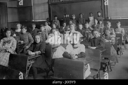 Full length landscape shot of schoolchildren seated at desks, African American students standing in the back, 1920. Stock Photo