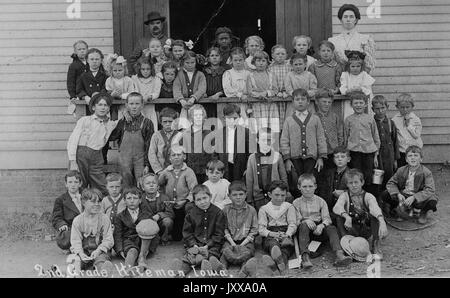 Full length landscape shot of schoolchildren seated and standing outdoors, African American students 'in last row as usual', 1920. Stock Photo