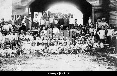 Full length landscape shot of schoolchildren seated and standing in rows outdoors, some African American, all wearing uniforms, 1920. Stock Photo