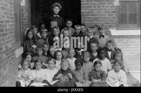 Full length landscape shot of schoolchildren, all seated with one female teacher, African American students integrated, 1920. Stock Photo