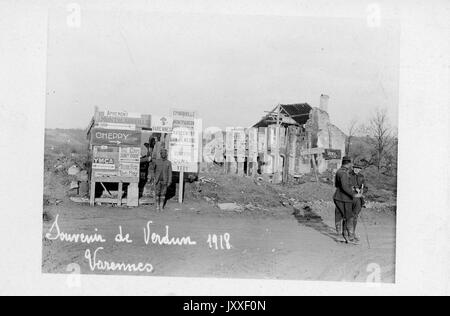 African American soldier standing in front of a board of signs in Cheppy, France after the Battle of Verdun that took place during World War I, two military men are standing to the side, there is a crumbling building in the background, France, 1918. Stock Photo