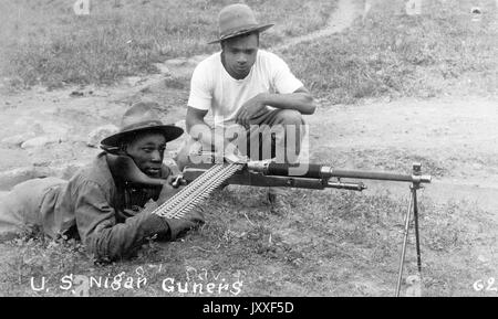 Two African American soldiers sitting with a gun, one is laying on the floor behind the gun focusing on the target, the other is crouching down next to the gun watching on, photo is titled US Nigar Guners, 1920. Stock Photo