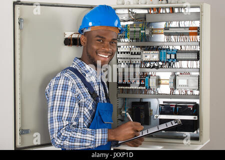 Male Technician Holding Clipboard While Examining Fusebox Stock Photo