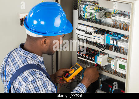 Young African Male Technician Examining Fusebox With Multimeter Probe Stock Photo