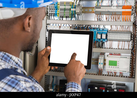 Close-up Of Young African Male Technician Using Digital Tablet While Examining Fusebox Stock Photo