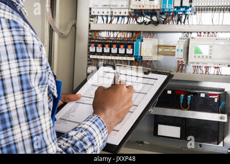 Close-up Of Male Technician Writing On Clipboard In Front Of Fusebox Stock Photo
