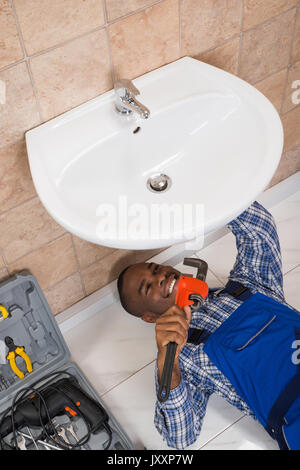 Happy Young African Male Plumber Fixing Sink In Bathroom Stock Photo
