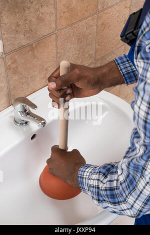 Close-up Of Plumber's Hand Using Plunger In Bathroom Sink Stock Photo