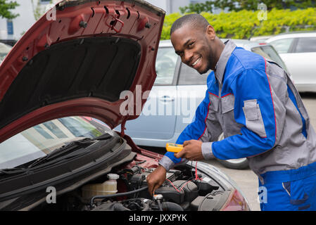 Happy Mechanic Using Multimeter To Check The Voltage Level In A Car Battery Stock Photo