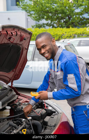 Happy Mechanic Using Multimeter To Check The Voltage Level In A Car Battery Stock Photo