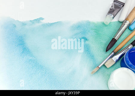 artist paintbrushes and paints over abstract hand painted watercolor background on textured paper Stock Photo