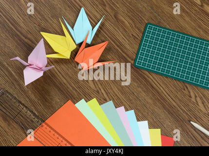 Origami cranes, colorful paper, cutting mat and pencil on wooden table Stock Photo