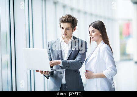 Couple discussing new project on the laptop atanding against in office room with panoramic windows Stock Photo