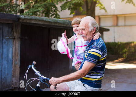 Grandpa riding bicycle with granddaughter in his hands Stock Photo