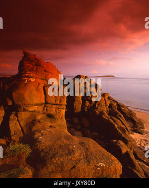 Dramatic evening sunlight strikes the sandstone rocks near Kildonan with Pladda Isle and lighthouse in view, Island of Arran Stock Photo