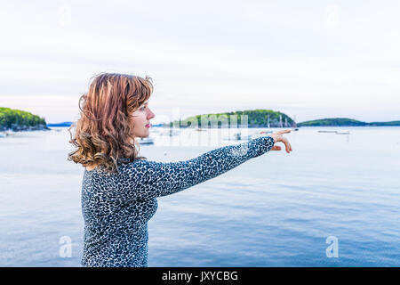 Young woman pointing to boats on edge of dock in Bar Harbor, Maine at sunset Stock Photo