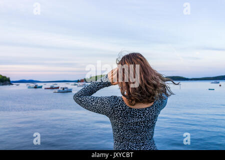 Young woman pointing to boats on edge of dock in Bar Harbor, Maine at sunset Stock Photo