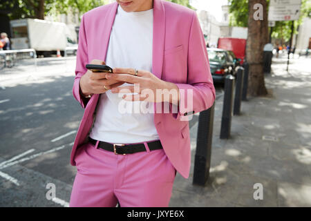 Mid section of man in baby pink suit using phone in street Stock Photo