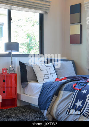 colorful bedroom with white and gray pillow on bed and gray lamp,alarm clock on the red sideboard Stock Photo