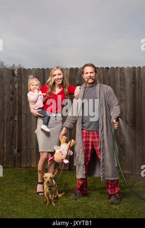 Caucasian couple posing near wooden fence with baby daughter Stock Photo