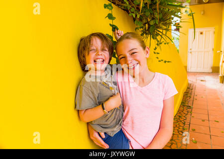 Caucasian girl leaning on yellow wall holding brother Stock Photo