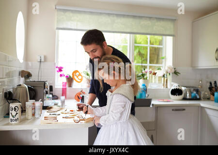 Father And Daughter Decorating Halloween Cookies Together Stock Photo