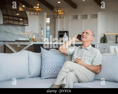 Caucasian man sitting on sofa talking on cell phone Stock Photo