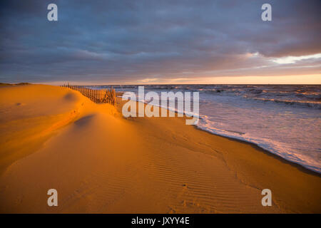 Ocean waves near sand dunes at sunset Stock Photo