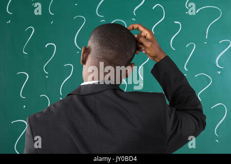 Rear View Of African Businessman In Front Of Chalkboard With Question Mark Sign Stock Photo