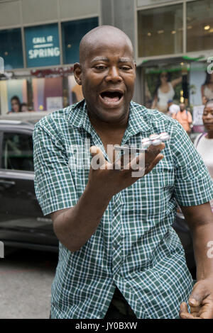 An expressive man selling fidget spinners demonstrates spinning several of them at one. In the Herald Square section of Manhattan, New York City. Stock Photo