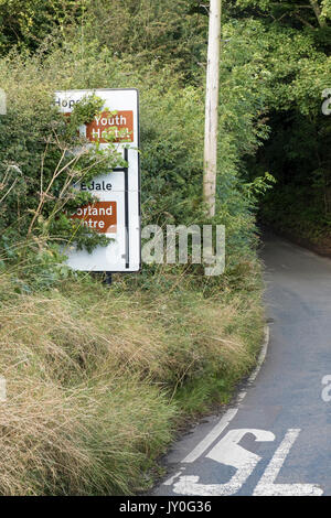 Obscured road sign, visibility blocked by an overgrown hedge or tree on a rural road near Edale, Derbyshire, England, UK Stock Photo