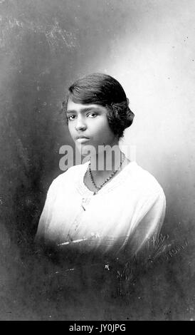 Portrait of the top half of a young African American woman, she is wearing a light colored top and a dark colored necklace, 1915. Stock Photo