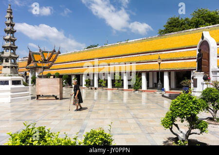 Old woman with walking stick walking across the courtyard at Wat Suthat Thepwararam, Bangkok, Thailand Stock Photo