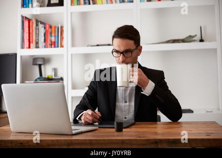 Caucasian businessman using laptop and digital tablet drinking coffee Stock Photo