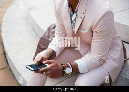 Mid section of a man in pink suit sitting using smartphone Stock Photo