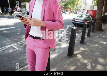 Mid section of man in baby pink suit using phone in street Stock Photo